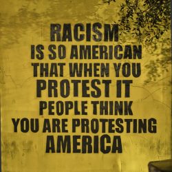 photo of a wall mural that states: Racism is so American that protest it and peple think you are prtesting America.